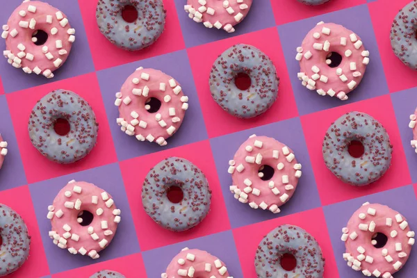 Μοτίβο από ντόνατς διακοσμημένα marshmallow και πολύχρωμα ψεκάζει σε τετράγωνο ροζ και μωβ φόντο. Επίπεδη. Στο πάνω μέρος. Ανθυγιεινά τρόφιμα — Φωτογραφία Αρχείου