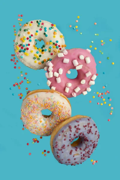 Birkaç donut dekore edilmiş marşmelov ve mavi arka planda uçuşan renkli şekerlemeler. Düz yatıyordu. Üst Manzara. Sağlıksız yiyecekler