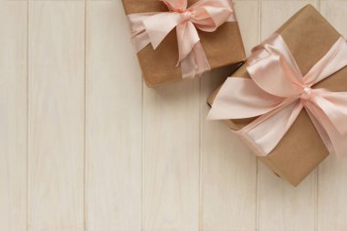 Kahverengi el işi kağıdına sarılı iki hediye kutusu ve beyaz ahşap arka planda pembe kurdeleler. Sevgililer Günü ya da Anneler Günü konsepti. Üst Manzara. Boşluğu kopyala