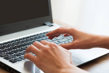 Genç yetişkin dizüstü bilgisayar kullanıyor ve klavyede daktilo kullanıyor. Yumuşak odaklanma. Evde bir iş. Kadın Serbest Çalışan.