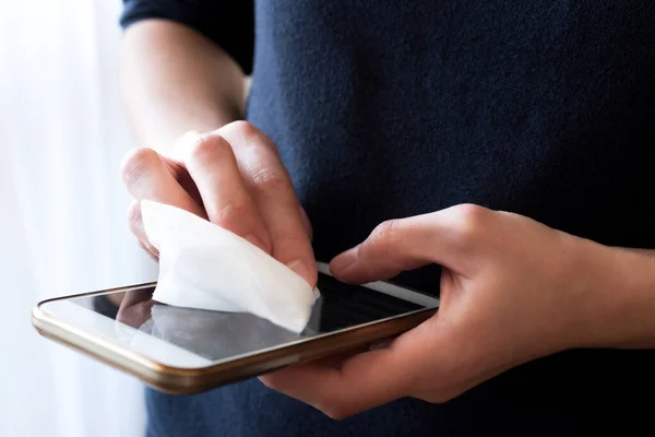 Female hands wipe smartphone screen with disinfectant napkin.