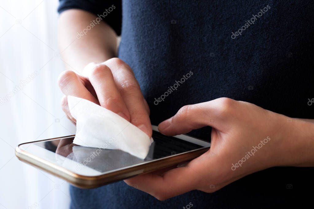 Female hands wipe smartphone screen with disinfectant napkin.