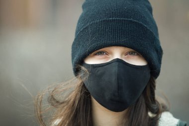 Kulak ilmeği maskeli, siyah şapkalı ya da şapkalı genç bir kızın portresi. Yaklaş. Siyah maskeli bir genç, dışarıda.