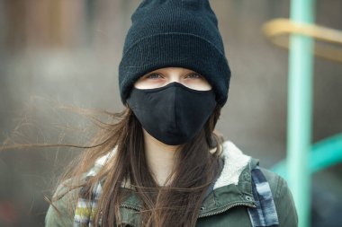 Kulak ilmeği maskeli, siyah şapkalı ya da şapkalı genç bir kızın portresi. Yaklaş. Siyah maskeli bir genç, dışarıda.