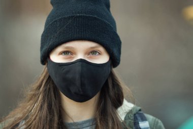 Kulak ilmeği maskeli, siyah şapkalı ya da şapkalı genç bir kızın portresi. Yaklaş. Siyah maskeli bir genç, dışarıda.