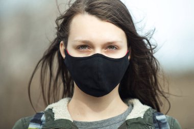 Siyah kulaklıklı genç bir kızın portresi. Yüzü siyah maskeli genç, dışarıda.