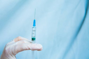 Beyaz eldivenli eller mavi arka planda bir şırınga tutuyor. Coronavirüs dezenfektanları, Asya gribi salgını, Coronavirüs 2019-nCoV, Corona virüsü salgını. Sprey şişesi.