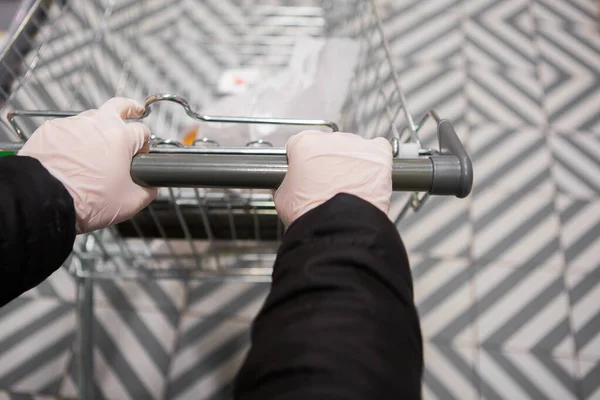 Beyaz eldivenli kız dükkanda bir araba yuvarlıyor. Salgın güvenliği. Eldivenli eller sepette