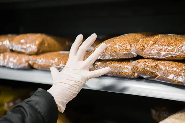Eldivenli bir el, salgın güvenliği için raftan bir paket karabuğday alır.