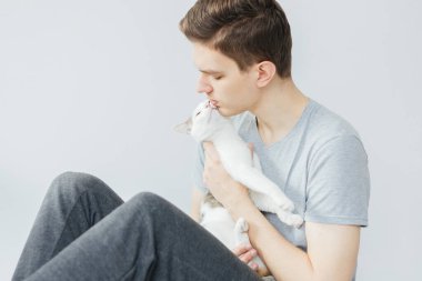 Açık gri arka planda kedisi olan genç bir adam. En sevdiği hayvan. Kediyi tutan adam