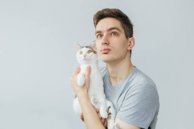 Açık gri arka planda kedisi olan genç bir adam. En sevdiği hayvan. Kediyi tutan adam