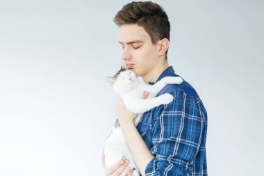 Açık gri arka planda kedisi olan genç bir adam. En sevdiği hayvan. Kediyi tutan adam