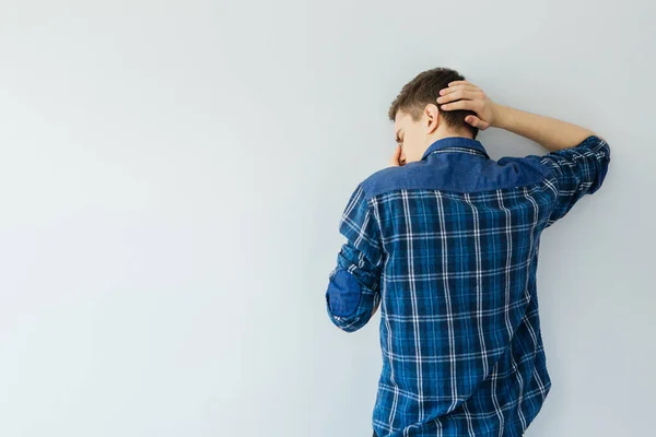 Mavi gömlekli genç bir adam duvara bakıyor. Depresyon, sorunlar ve stres