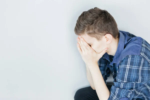 Genç bir adam elleriyle yüzünü kapatıyor. Sorunlar ve stres. Açık gri arka planda üzgün bir adam