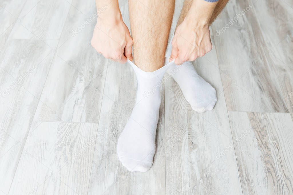 man puts white socks on a gray wooden floor in the room