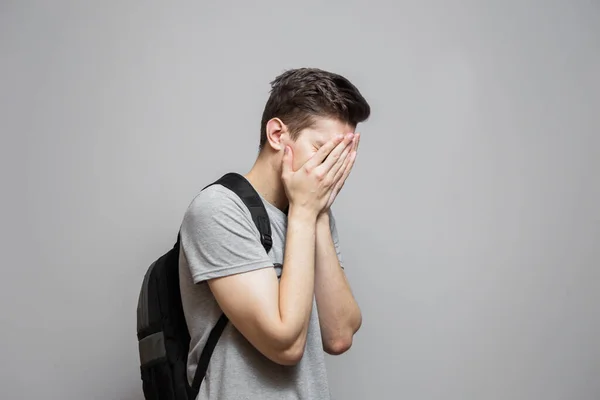 Gri gömlekli genç adam elleriyle yüzünü kapatıyor. Gri arka plandaki adam