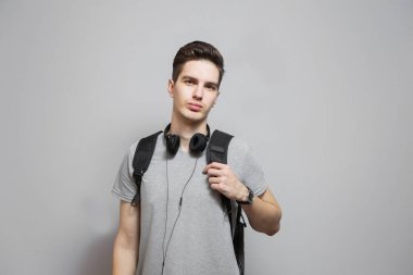 Gri arka planda kulaklıklı sırt çantalı genç bir adam. Çantalı öğrenci müzik dinliyor..