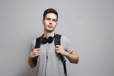 Gri arka planda kulaklıklı sırt çantalı genç bir adam. Çantalı öğrenci müzik dinliyor..