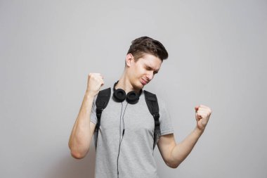 Gri arka planda kulaklıklı sırt çantalı genç bir adam. Çantalı öğrenci müzik dinliyor..