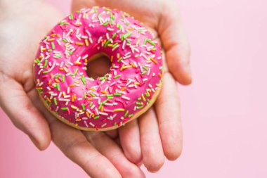 Pembe arka planda pembe çörek. Pembe çörek tutan kadın.