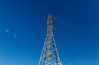 Mavi gökyüzü arka planında mavi yüksek voltaj kulesi. Şehirde elektrik hatları var.. 