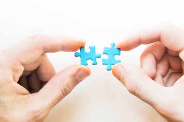 Mavi bulmaca elinde. Beyaz arka planda bulmaca parçasıyla el ele tutuşmak. Yapboz, iş bağlantısı, eğitim, toplum ve takım çalışmasına bağlanıyor