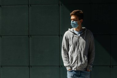 Yeşil bir duvarın arka planında Coronavirus 'tan gelen tıbbi maskeli genç adam. 