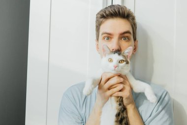 Genç adam evde bir kediye sarılıyor. Kedili genç adam.