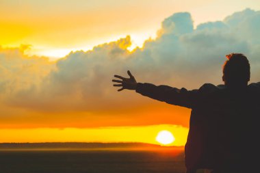 Güzel günbatımında sahada bir adam. Kollarını açmış genç bir adamın silueti.