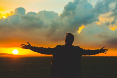 Güzel günbatımında sahada bir adam. Kollarını açmış genç bir adamın silueti.