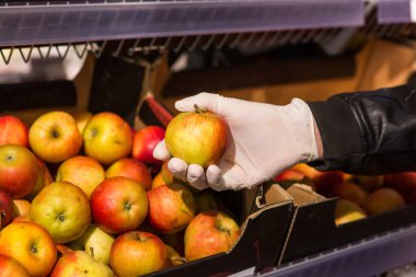 Dükkanda beyaz eldivenli bir adam yiyecek satın alır. Elma tutan adam