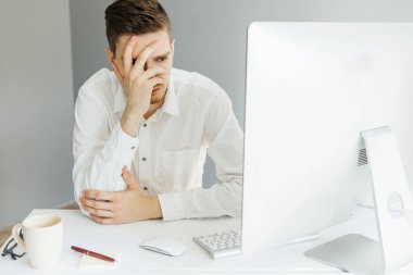 Ofiste bilgisayarla çalışan beyaz gömlekli genç bir adam. Gri arkaplanda çalışan işçiler