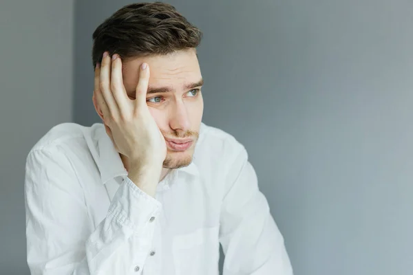 Ofisinde bilgisayarla birlikte beyaz gömlekli genç bir adam masaüstünde oturuyor. Gri arkaplanda çalışan işçiler