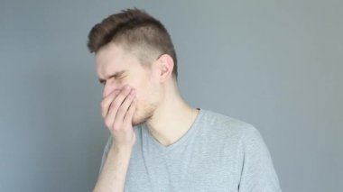 Gri arka planda gri gömlekli genç hasta adam tıbbi maske takıyor.