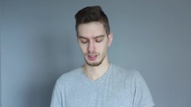 Gri gömlekli genç adam gri arka plandaki spor sırasında şişeden su içiyor.