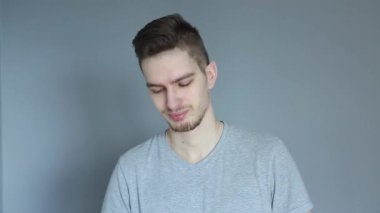 Gri gömlekli genç adam gri arka plandaki spor sırasında şişeden su içiyor.