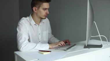 Ofiste bilgisayarla çalışan beyaz gömlekli genç bir adam. Gri arka planda çalışan bir işçi. Kafasını tutan adam