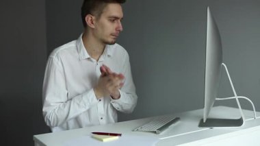 Ofiste bilgisayarla çalışan beyaz gömlekli genç bir adam. Gri arkaplanda çalışan işçiler