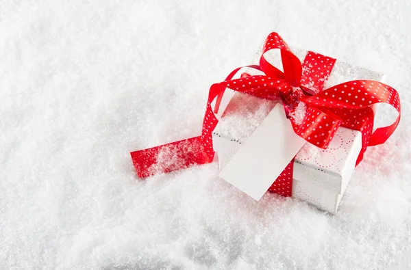 Geschenkkarton mit roter Schleife und Schleife mit Notizpapier auf Schnee Stockbild