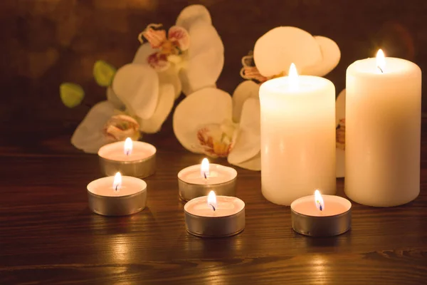 Burning candles and orchid flowers on dark background — Stock Photo, Image