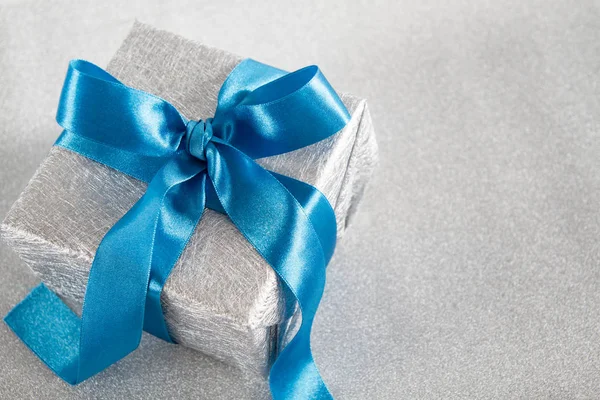 Silver gift box with blue ribbon on silver background