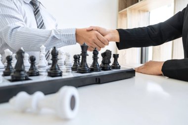 İş adamı ve iş kadını satranç oynadıktan sonra el sıkışıyor ve strateji çöküşünü düşünüyor karşı takımı deviriyor ve galibiyet ve başarı için geliştirme analizi yapıyor..