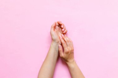 Kadının elleri kozmetik kremi nemlendiriyor. Pembe arka planda fotokopi alanı, güzellik ve bakım konseptiyle losyon sürüyor. Kalıp düz üst görünüm yatıyordu