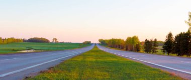 Şafak sökerken kırsal bir çayırda ve kırsal bir yolda. Şehir fotokopi alanının arkasındaki kırsal alan güneşi ufukta beliriyor.