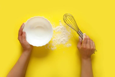 Mutfak aletlerini tutan kadın eller, süzgeç, merdane, kase, süzgeç, fırça, çırpma, sarı arka planda yemek pişirme. Gıda çerçevesi, kopyalama alanı ile pişirme kavramı. Düz görünüm afişi serildi