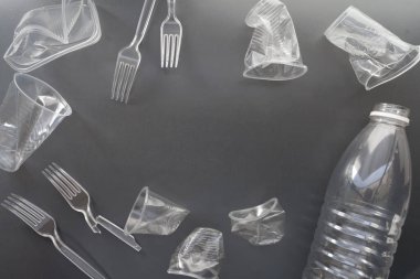 Geri dönüşüm için kullanılan plastik şişeler, bardaklar, çatal bıçak takımı ve çantalar, gri arka planda geri dönüşüm atığı, ekoloji, arazi kirliliği kavramı