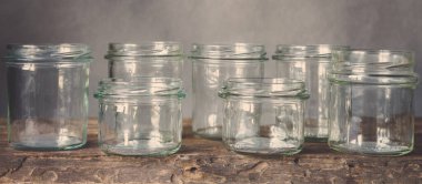 Tahta bir masada, cam kavanozlarda sağlıklı yiyecekler pişirmek için çeşitli çiğ tahıllar, taneler, fasulyeler ve makarna. Gri arka planda, temiz yemek, vegan, dengeli diyet, sıfır atık, çevre dostu, plastiksiz.