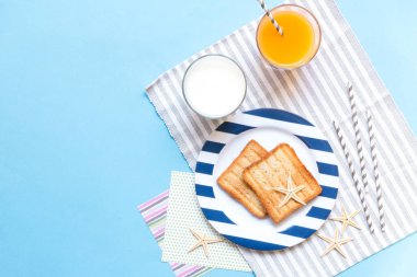 Breakfast toast, orange juice, water for children in the marine theme, creative with shells on a blue background