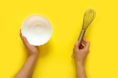Mutfak aletlerini tutan kadın eller, süzgeç, merdane, kase, süzgeç, fırça, çırpma, sarı arka planda yemek pişirme. Gıda çerçevesi, kopyalama alanı ile pişirme kavramı. Düz görünüm afişi serildi
