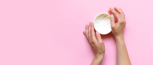 Woman's hands moisturizing cosmetic cream, lotion on a pink background with copy space, beauty, care concept. Pattern flat lay top view long banner